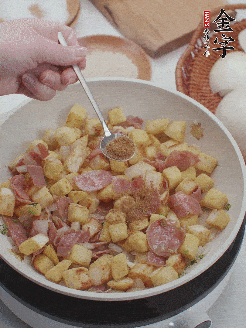 起鍋少油，煸香洋蔥丁、蔥白，加入金字培根火腿翻炒幾下，再加入饅頭丁、1小勺孜然粉、少許鹽翻炒均勻并鋪平。